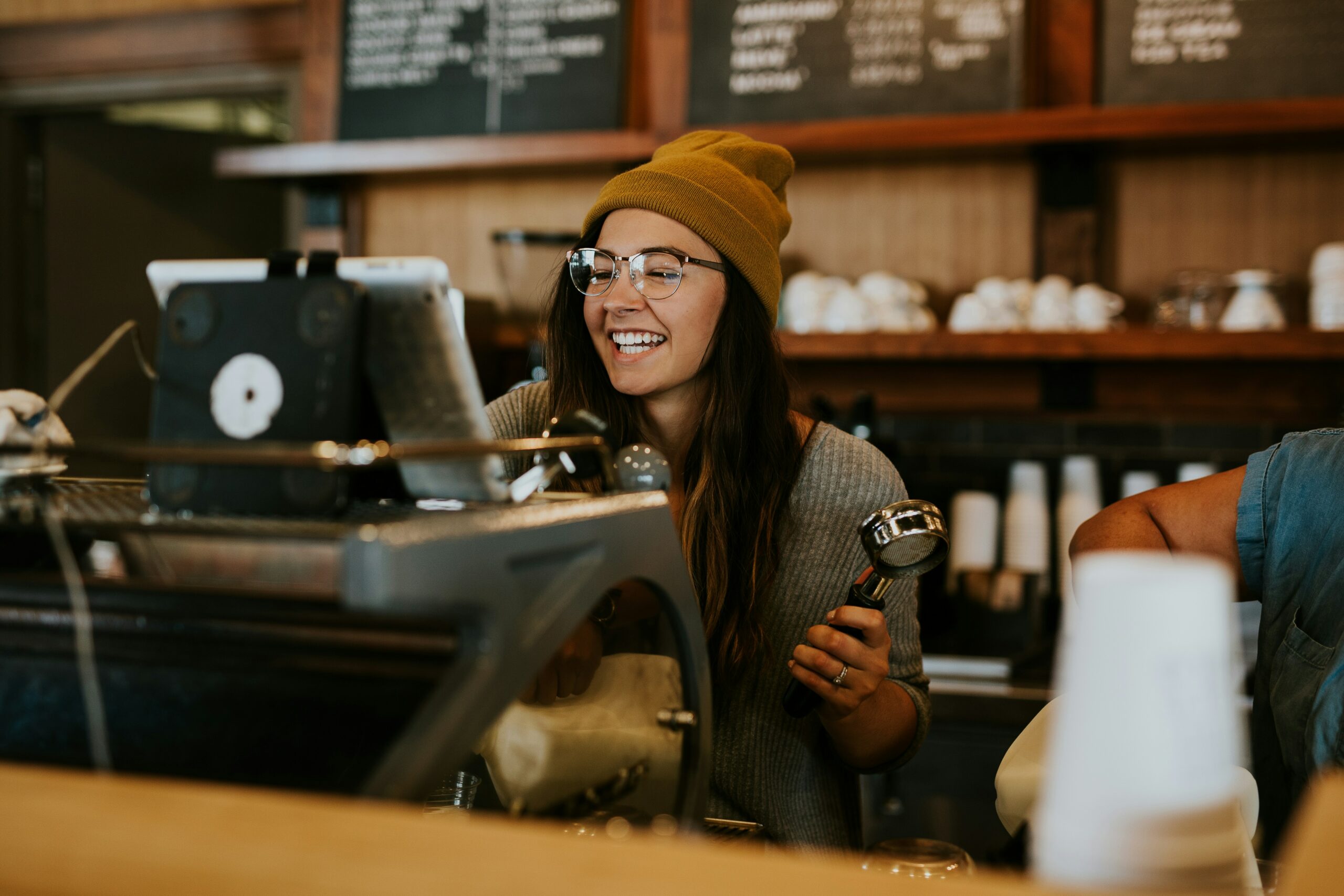 Dans un café, une serveuse sourit et prépare une commande derrière le comptoir.