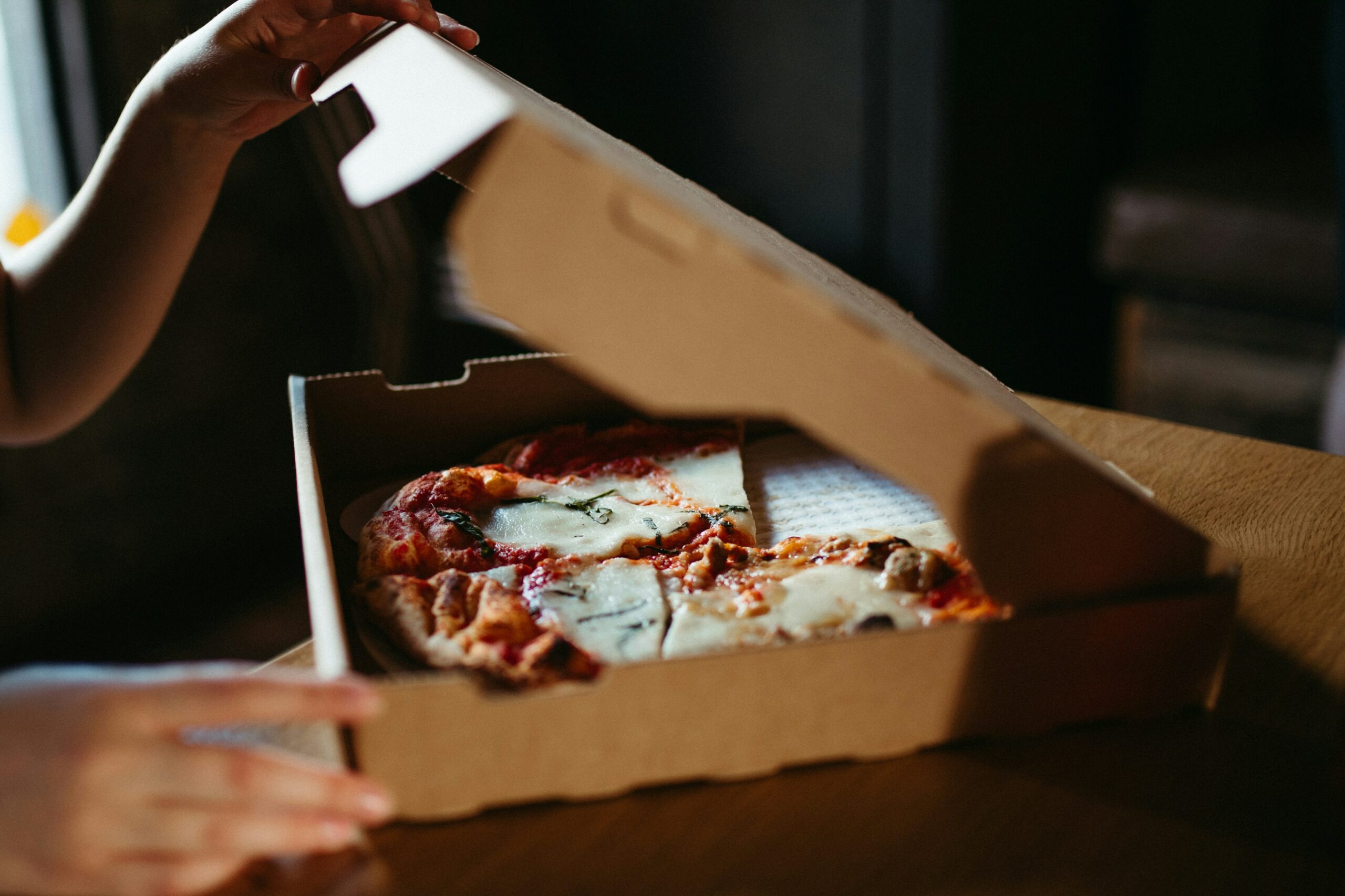 Un cliente apre la scatola di cartone della pizza ordinata tramite Click & Collect in una pizzeria.