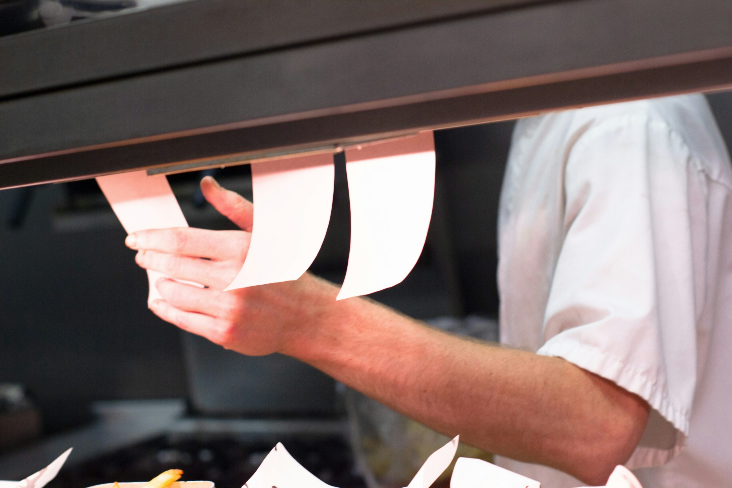 Cette photo montre un équipier en train de gérer les bons de commande dans une cuisine de restaurant.