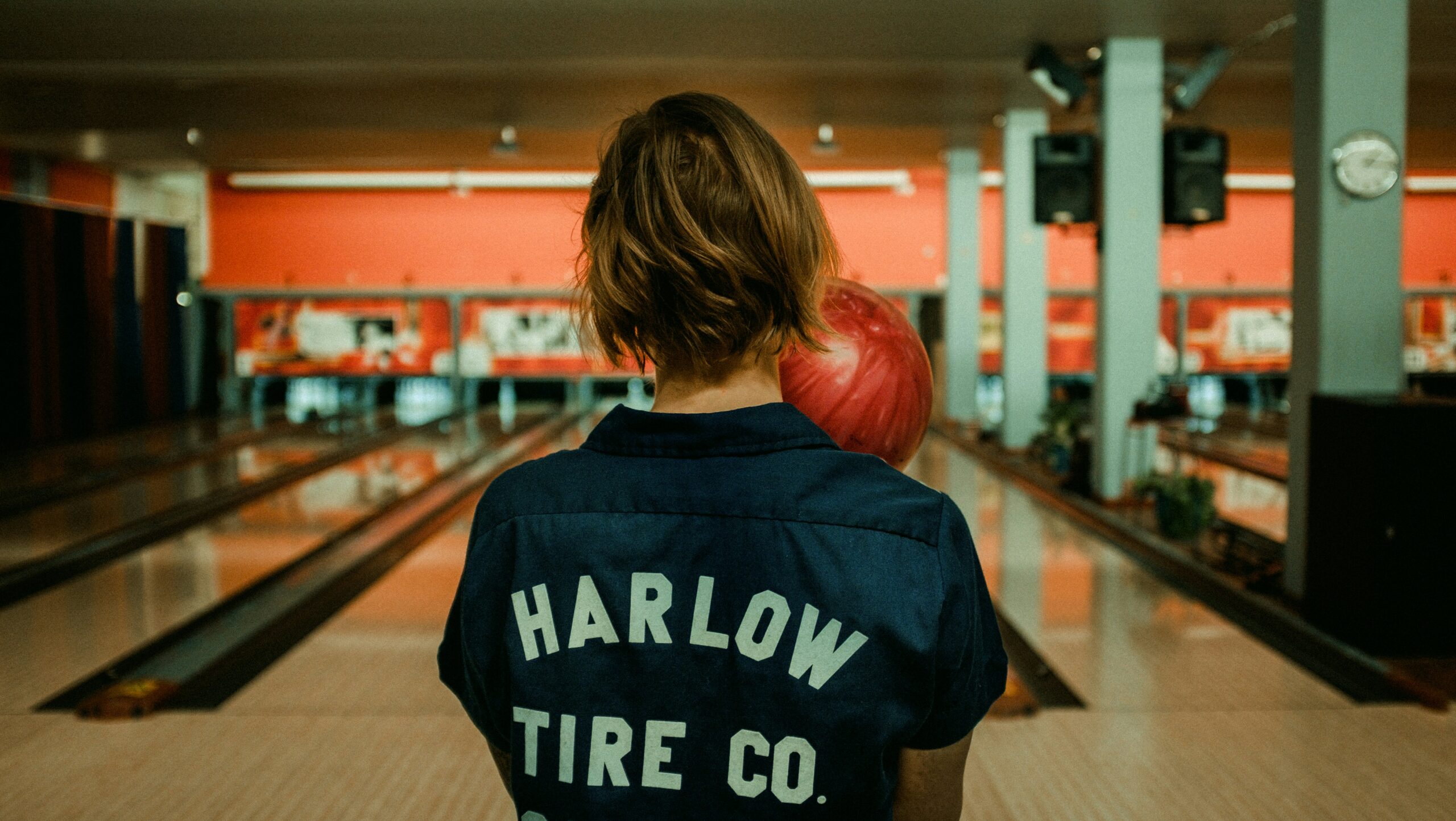 Image d'une personne sur des pistes de bowling, de dos, tenant une boule de bowling, s'apprêtant à lancer