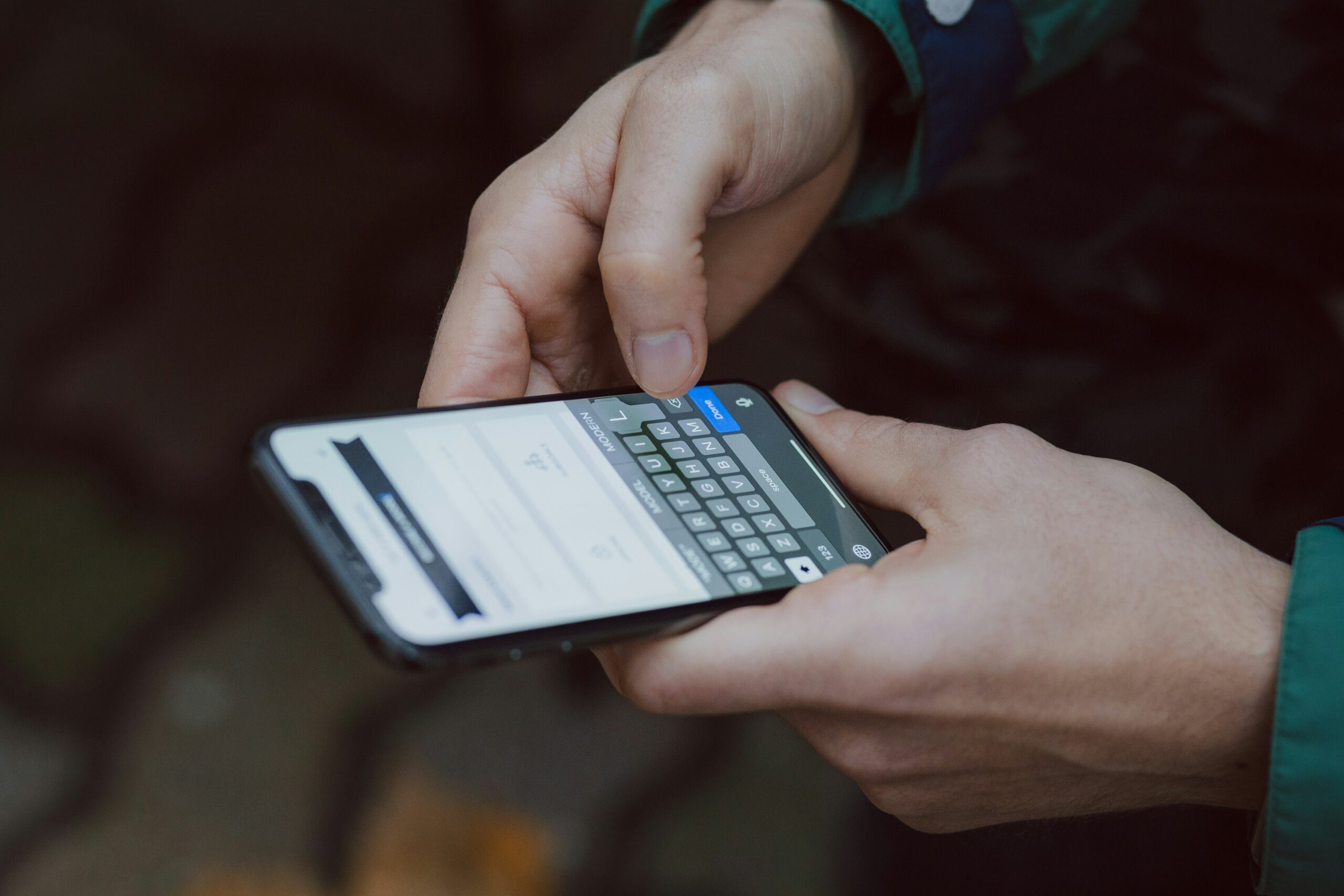 La photo montre une personne qui utilise son smartphone, tapant sur le clavier pour remplir un formulaire.