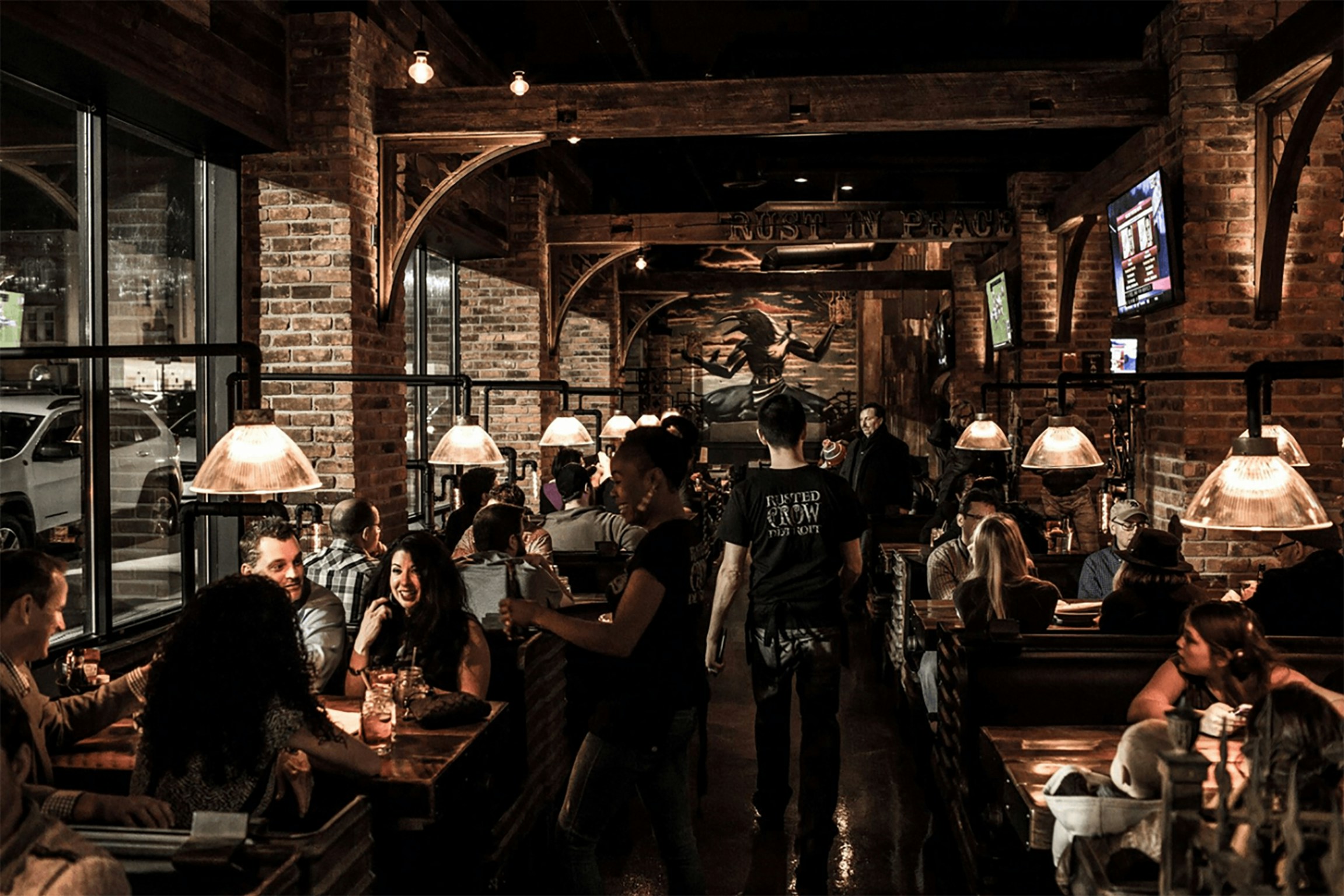 La photo montre l’intérieur d’un restaurant avec des tables occupées par des clients et un serveur en mouvement dans l’allée centrale.