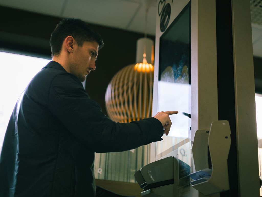 La photo montre un homme en train de passer commande sur une borne tactile dans un fast-food.