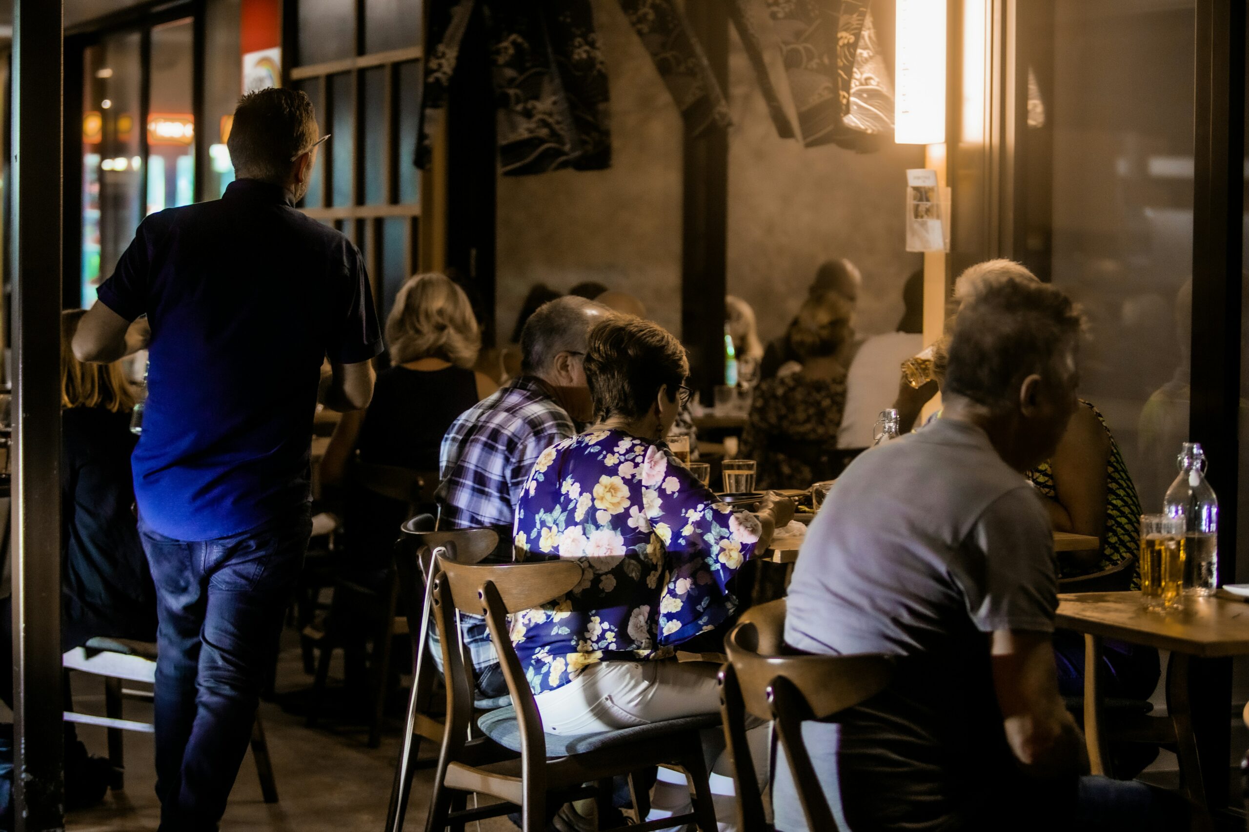 La photo montre la salle d’un restaurant où plusieurs clients mangent pendant qu’un serveur s’assure que tout se passe bien.